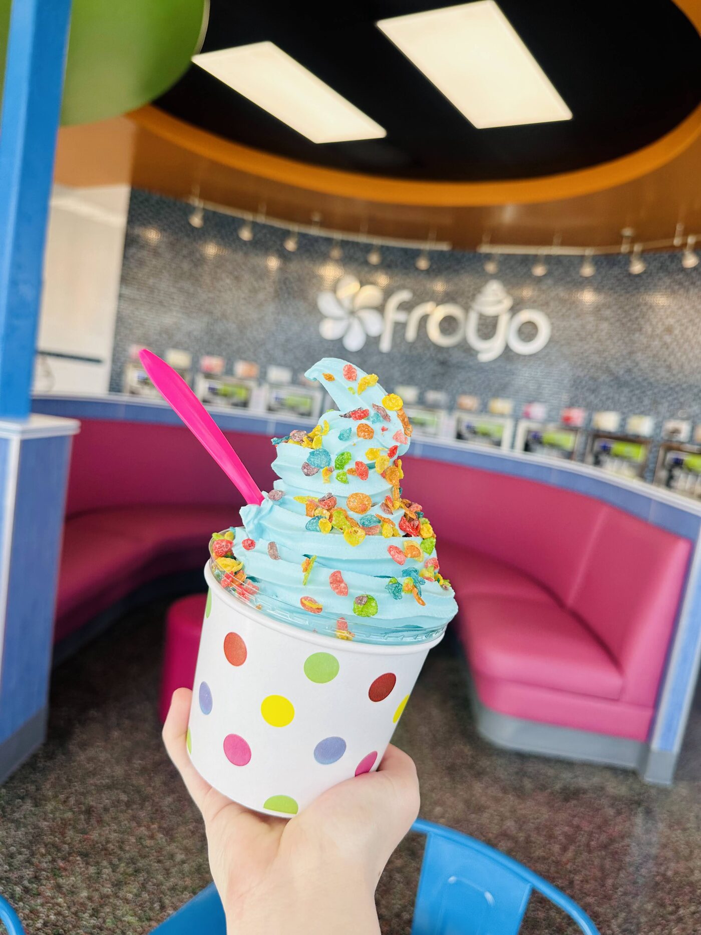 Polka-dot cup of swirled froyo piled with sprinkles, gummies, and fruit